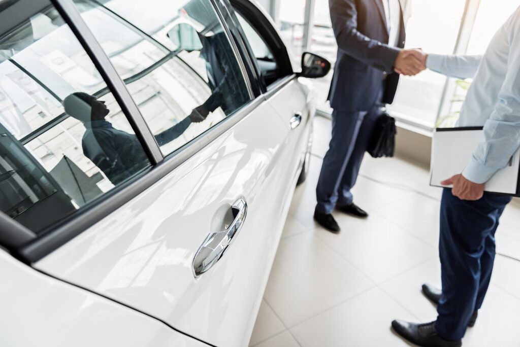 自動車の横で握手している2人の人