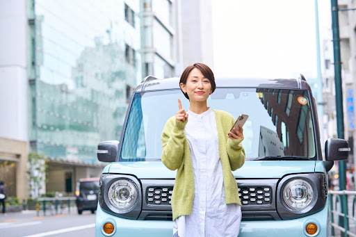 車の前に立ってスマホを持つ女性