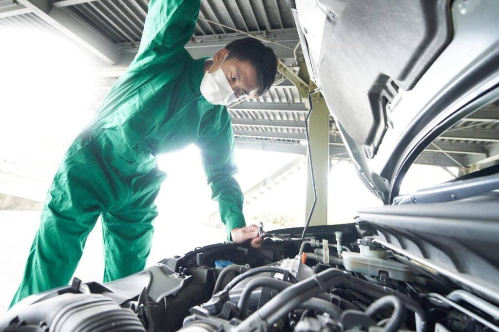 車を整備する緑色のつなぎを着た男性