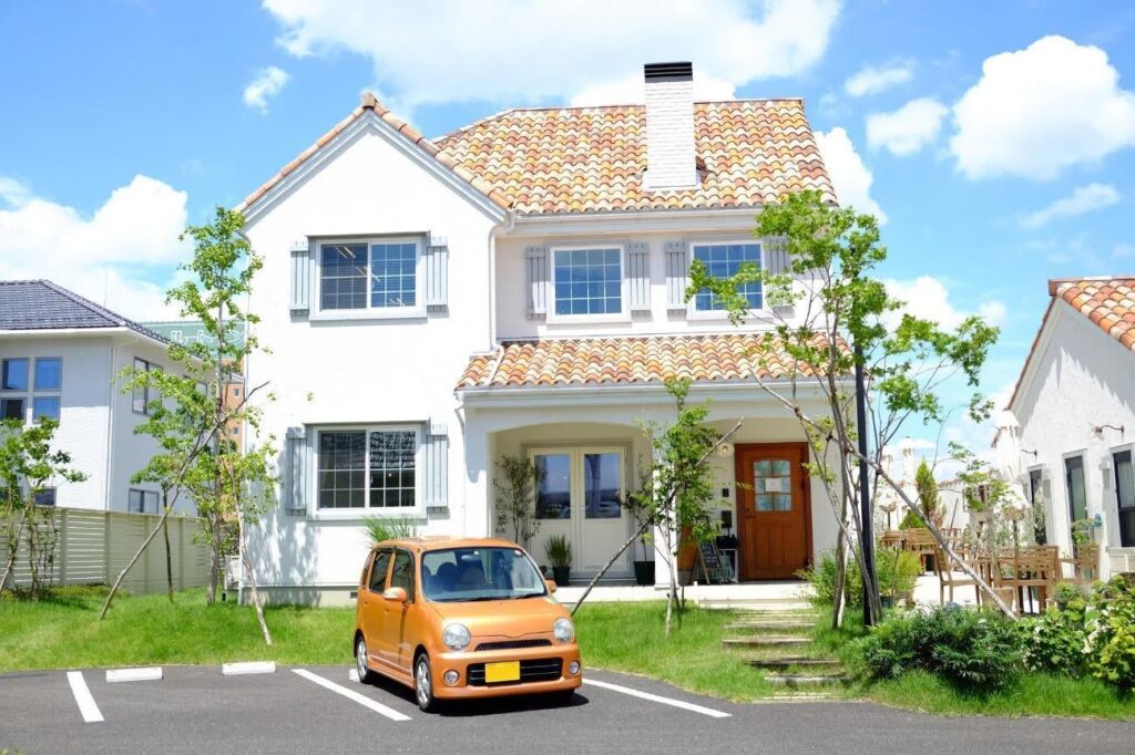 洋風の立派な一軒家と駐車場に停車したオレンジ色の軽自動車