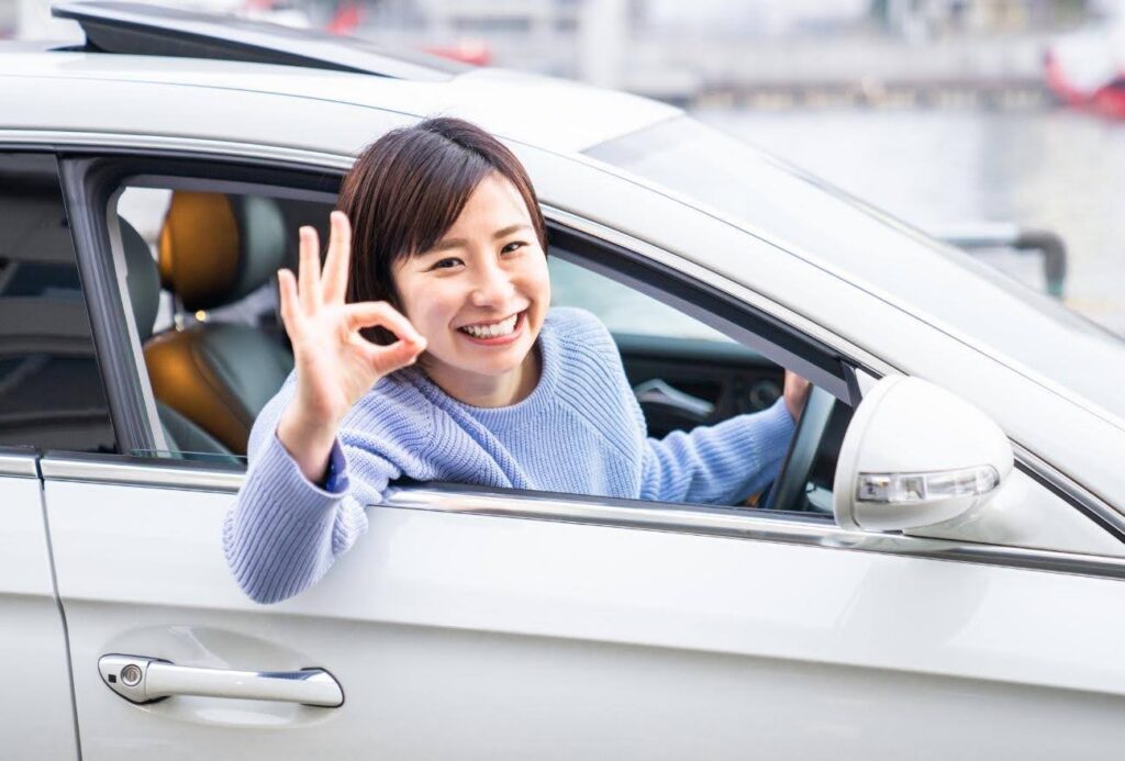 運転席から乗り出してOKサインを見せる笑顔の女性