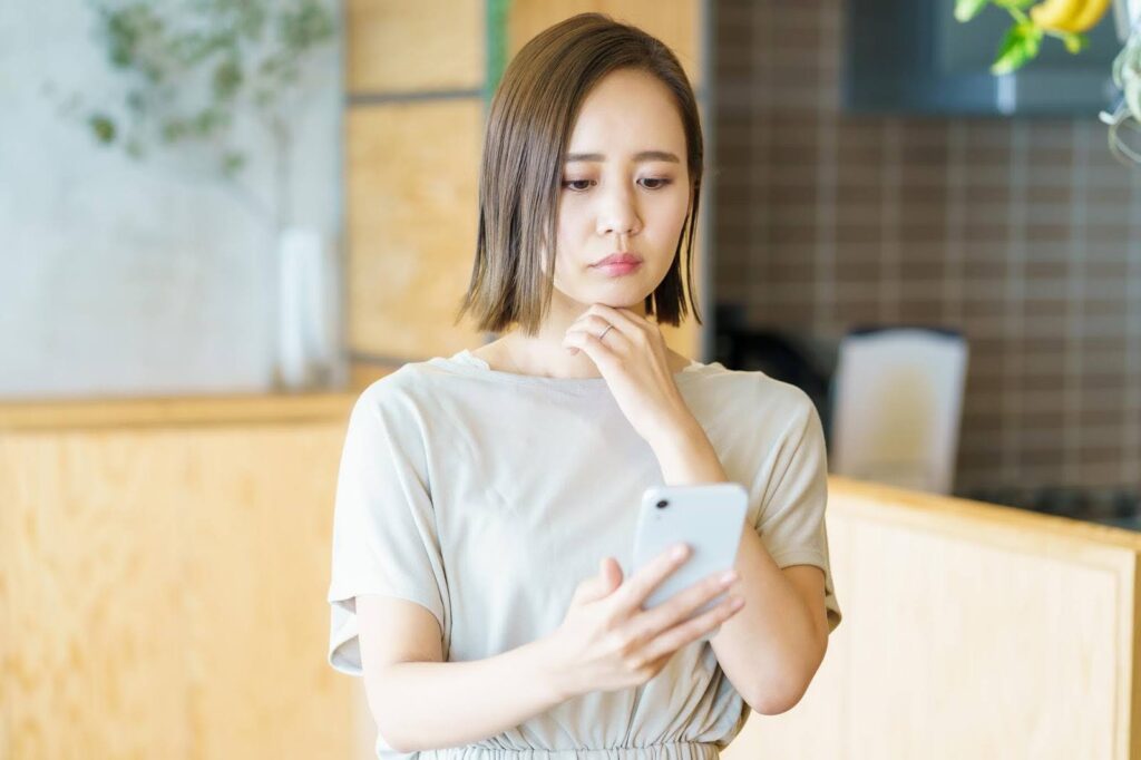 スマートフォンの画面を見て考え事をする若い女性