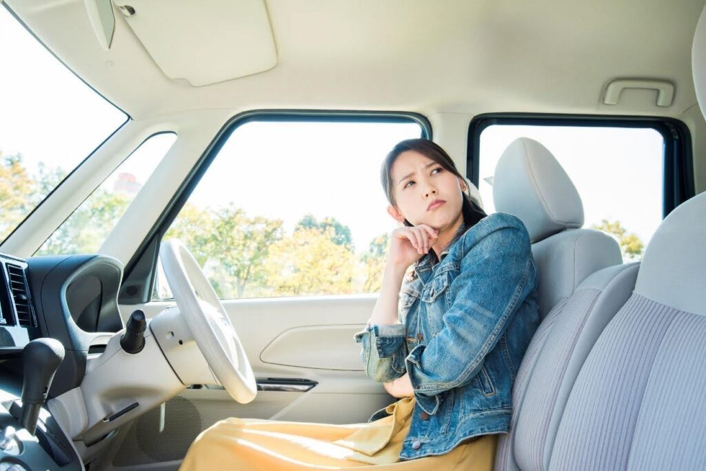 車内で運転席に座りながら考え事をする女性