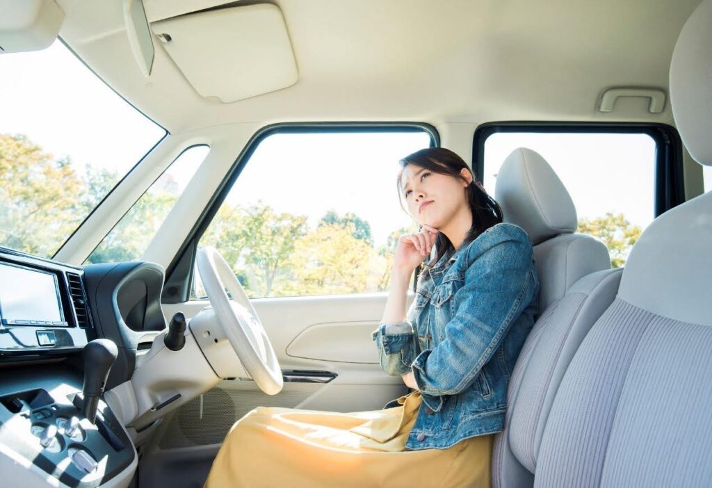 車の運転席で頭を傾けるデニムジャケットを着た女性