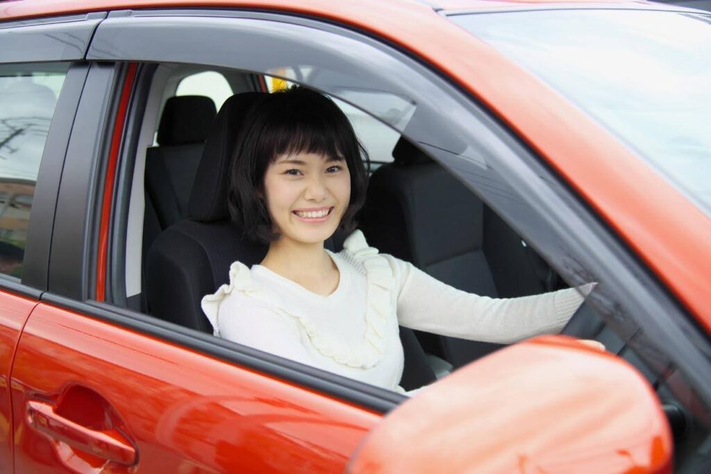 赤い乗用車の運転席から笑顔を見せる白い服装の女性