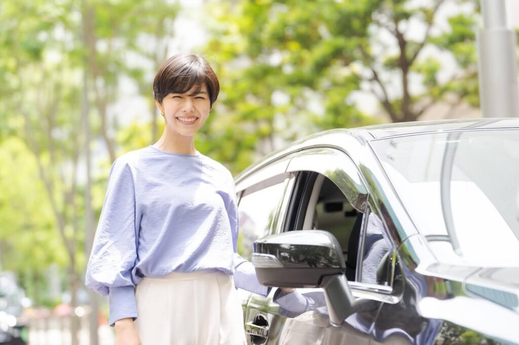 車の横に立ってほほ笑む若い女性
