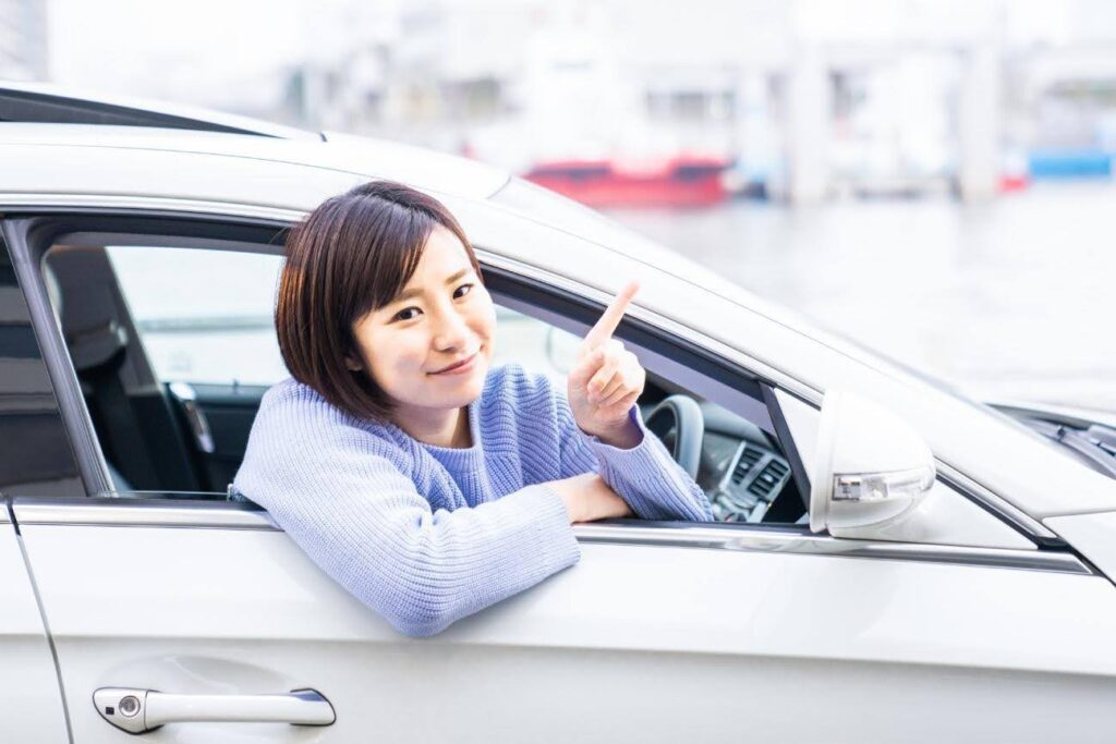 運転席から乗り出して人さし指を立てる青い服の女性