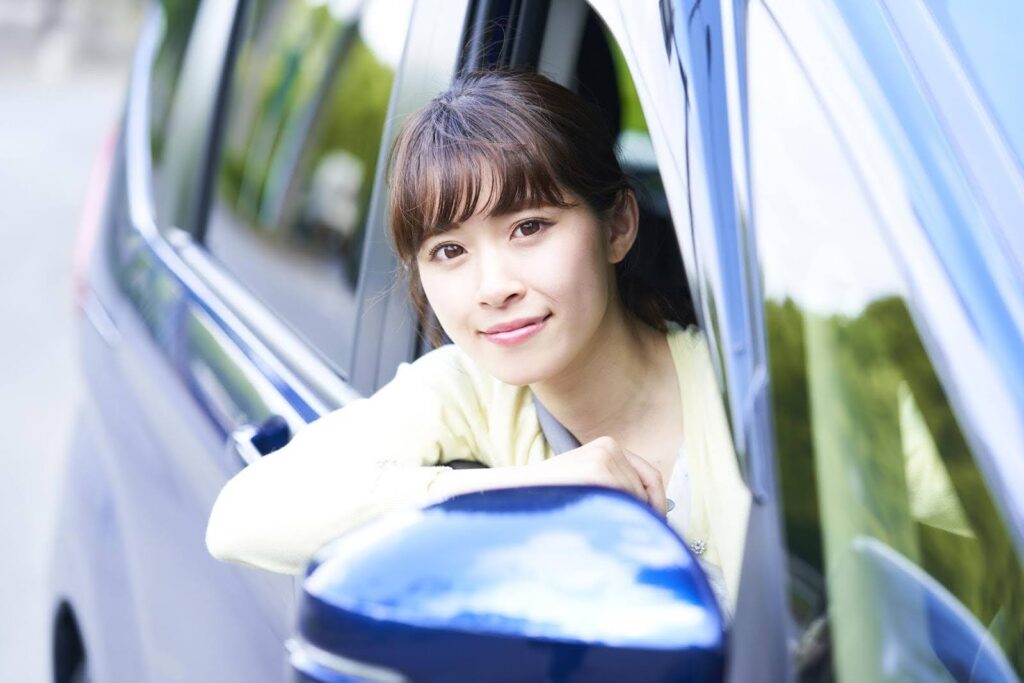 車の運転席から顔を出す笑顔の若い女性