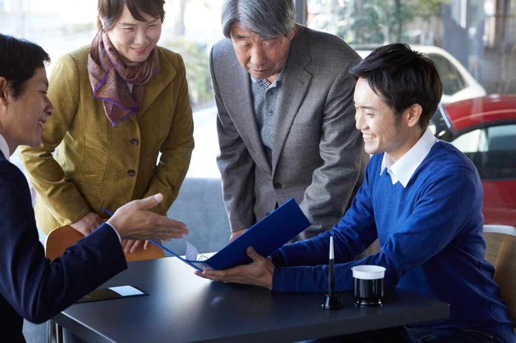 自動車販売店で商談する家族とビジネスマン