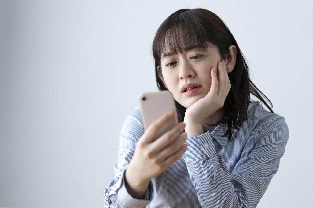 スマートフォンを見て困った顔をする若い女性