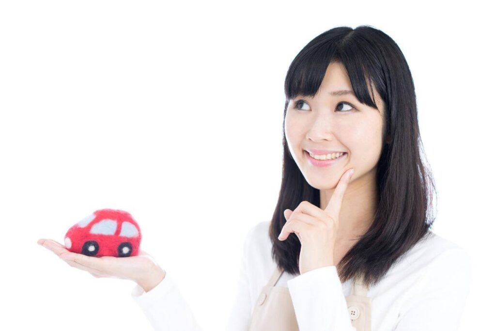 手のひらに赤い車のおもちゃを乗せながら右上を見上げる女性