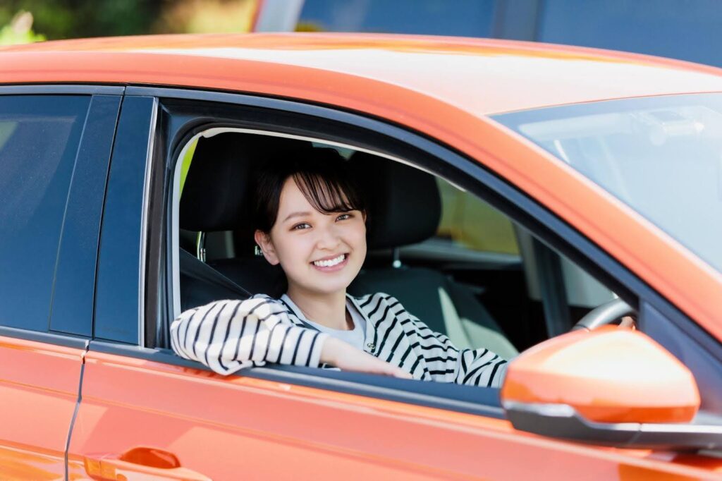 車の運転席から顔を出す笑顔の若い女性
