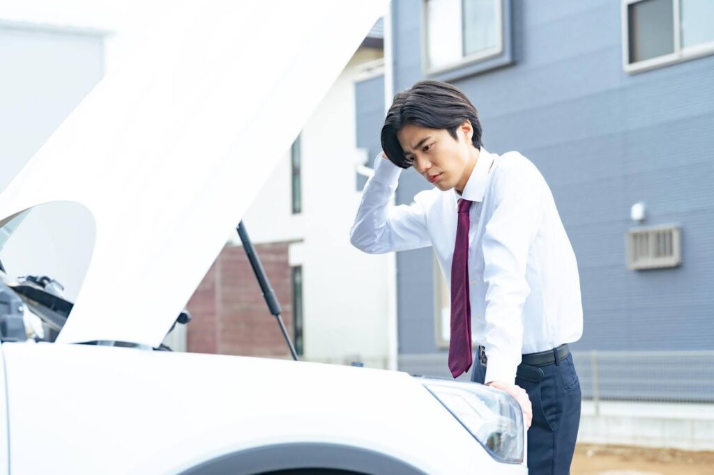 車のボンネットを開けて頭を抱える若い男性