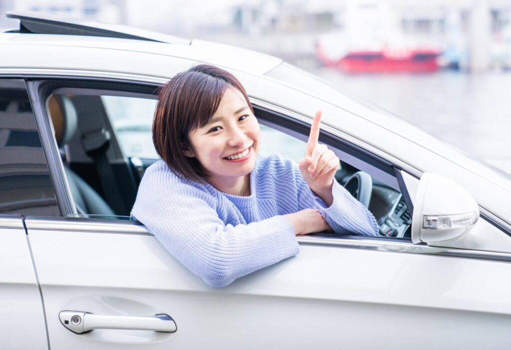 車の窓から顔を出す笑顔の若い女性
