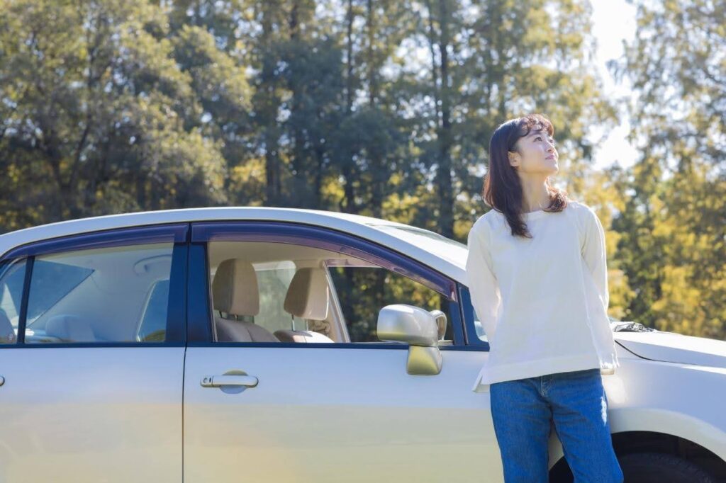 森林の中に車を停車して空を見上げる女性