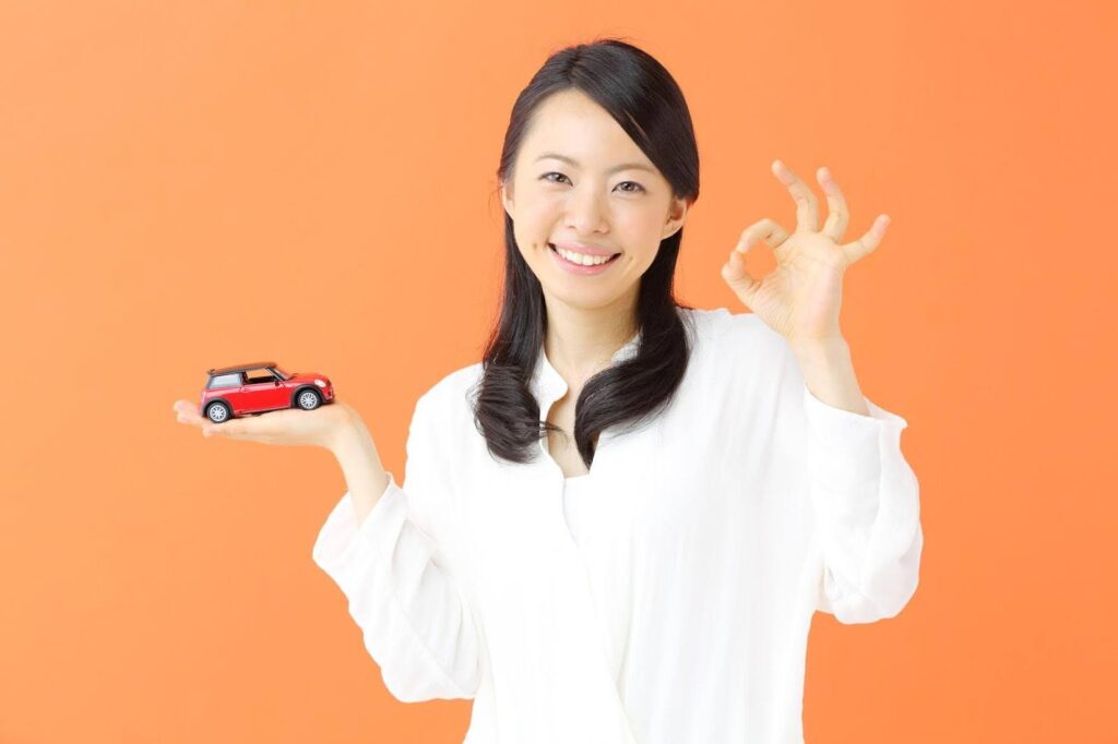 手でOKマークを作るミニカーを持った若い女性