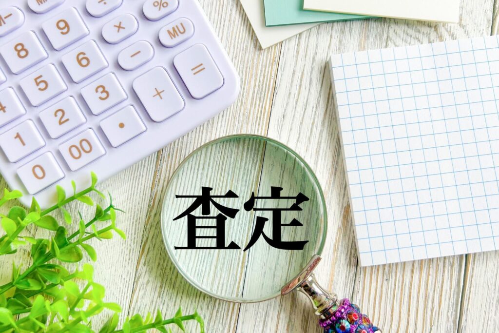 査定の文字を映す虫メガネと電卓やメモ帳